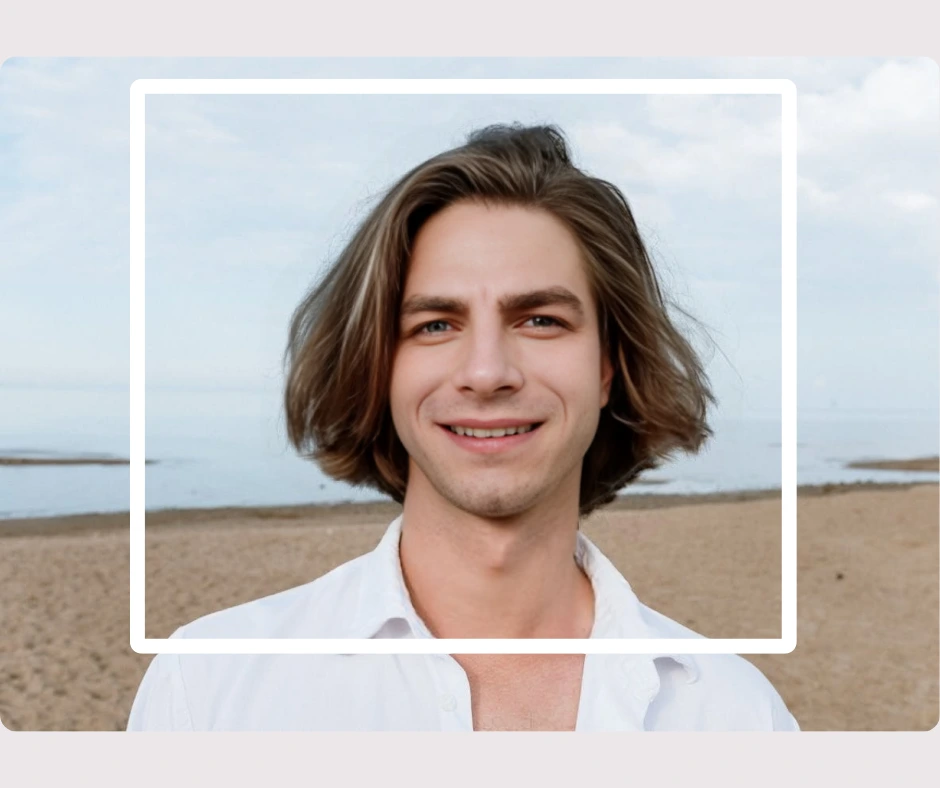 An image of a young man with long hair and white shirt on a beach smiling